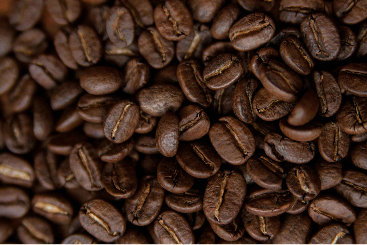 A close-up, top-down view of roasted coffee beans filling the entire frame, showing their rich dark brown color and characteristic crevices.